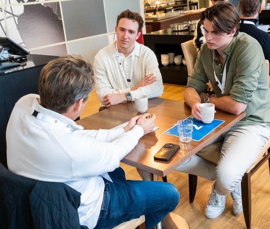 Drie mensen in gesprek aan een tafel met koffie